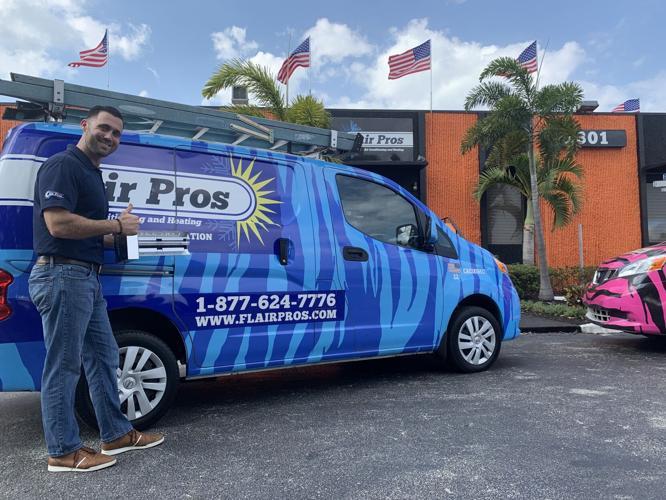 A man stands next to an Air Pros USA service van in a parking lot outside an orange building with American flags and palm trees—a proud moment for the team recently named Business of the Year by South Florida Business Journal.