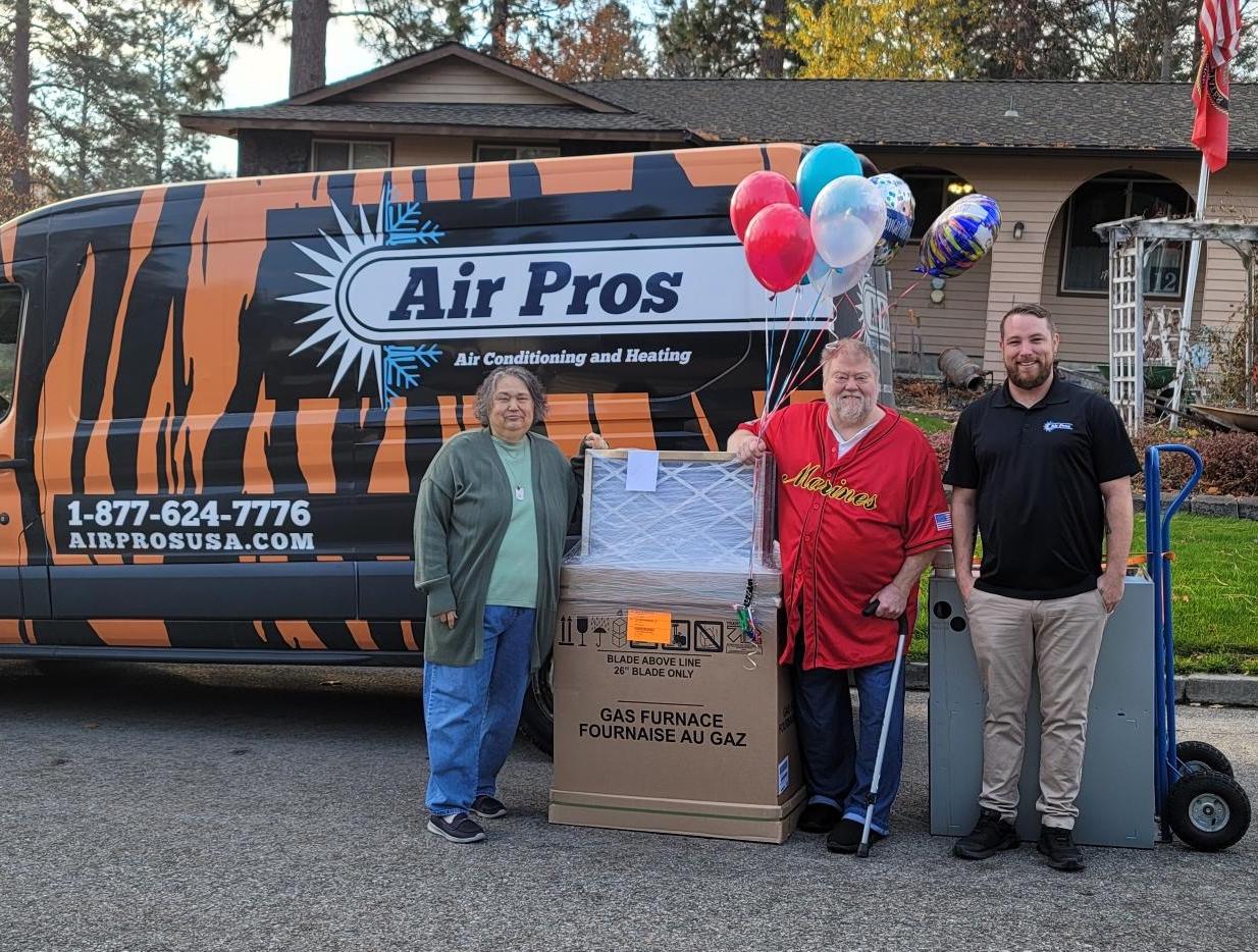 Three people stand in front of an Air Pros van and a house in the Spokane Area, posing with a new gas furnace, balloons, and a dolly.
