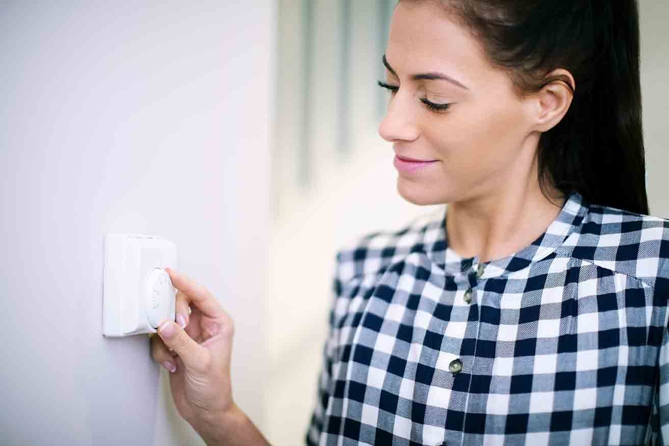 A woman in a checkered shirt adjusts her smart thermostat, making a quick thermostat upgrade with just a touch.